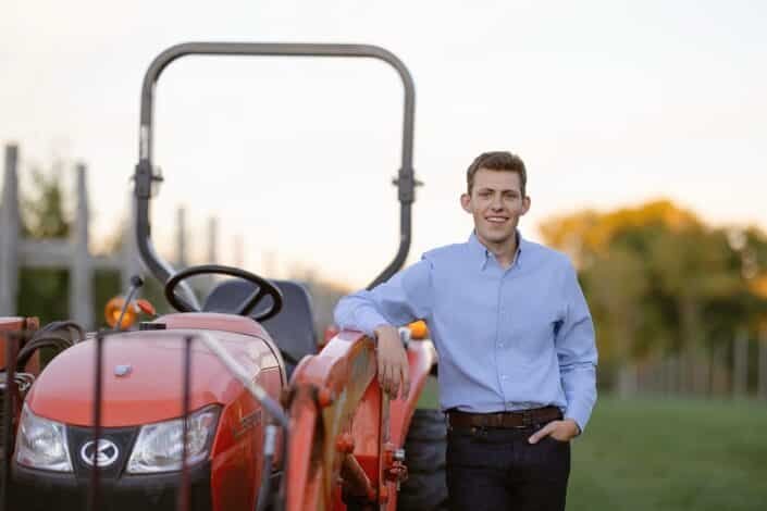 Farm owner standing beside a tractor in an organic apple orchard.